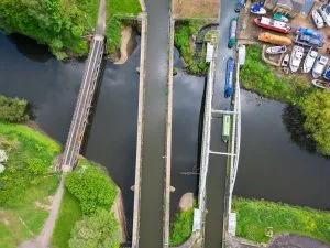 Aerial view of a canal lock system with boats, pathways, and greenery on either side.