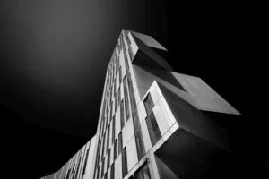 Black and white photo of a modern, angular skyscraper against a dark sky, emphasizing the structure's geometric design.